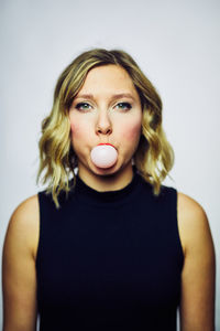 Close-up of woman blowing bubble gum against white background