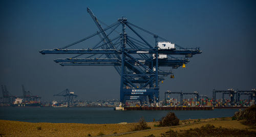 Cranes at commercial dock against clear blue sky