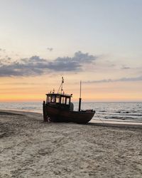 Fishing boat on beach against sky during sunset