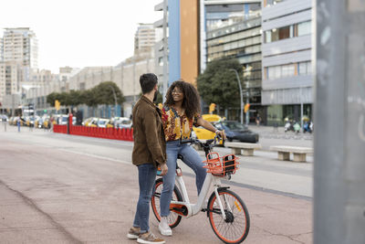 Young man with girlfriend sitting on bicycle at footpath