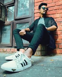 Young man sitting on street against wall