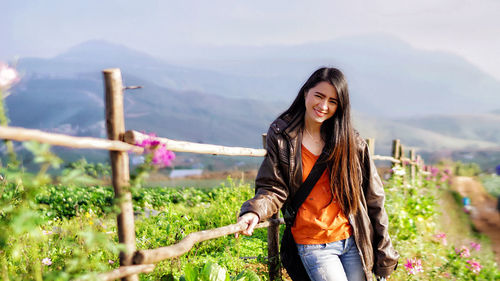 Portrait of smiling woman while standing on mountain by railing