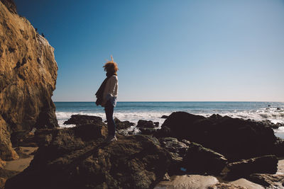 Woman standing on rock by sea against clear blue sky