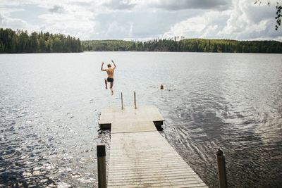 People on pier by lake against sky