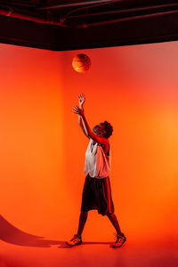 Full length of man with arms raised standing against orange sunset sky