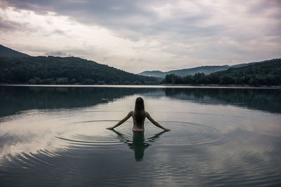 Rear view of woman standing in lake against cloudy sky