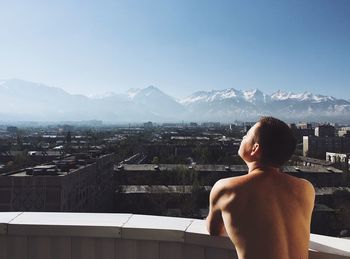 Rear view of shirtless man looking at cityscape against sky