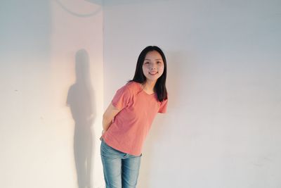 Portrait of smiling young woman standing against wall