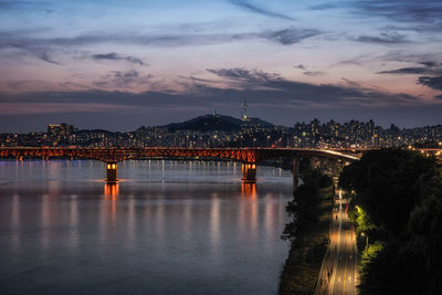 Illuminated bridge over river against sky at sunset