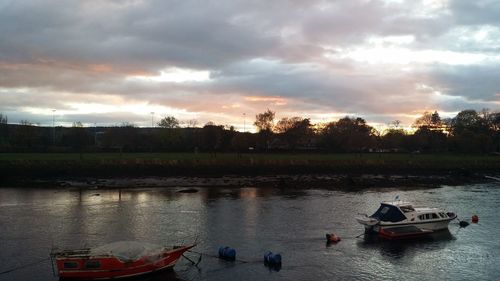 Boats moored on river against sky at sunset