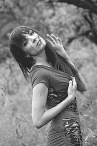 Portrait of sensuous young woman touching breasts while standing by plants