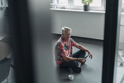 Smiling businessman using digital tablet while sitting on floor at office