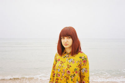 Portrait of beautiful mid adult woman standing at beach against clear sky