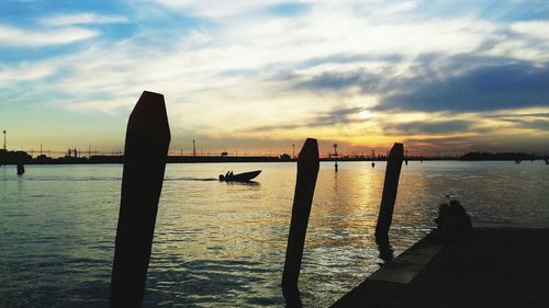 Silhouette wooden posts in sea against sky during sunset