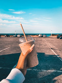 Close-up of hand holding drink at sea against sky