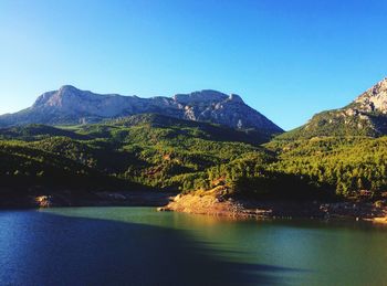 Scenic view of lake and mountains against clear blue sky