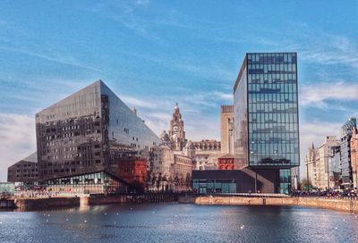 View of buildings by river against blue sky