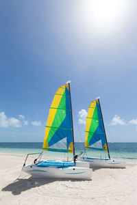 Sailboats on beach against cloudy sky