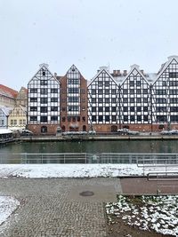 Buildings by river against sky in city during winter