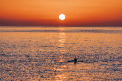 Silhouette people on sea against orange sky