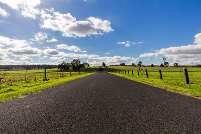 Road by agricultural field against sky