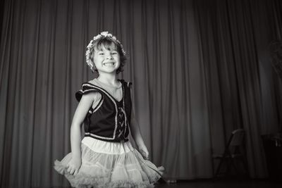 Portrait of happy girl standing against stage curtain