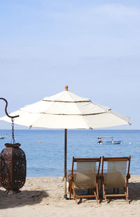 Deck chairs on beach against sky