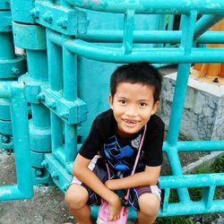 High angle portrait of smiling boy sitting on metallic play equipment