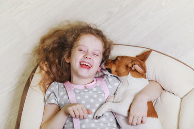 Laughing girl hugging and kissing a dog, lying on wood background.