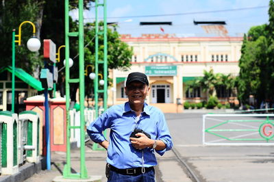 Portrait of senior man holding camera on road against built structure