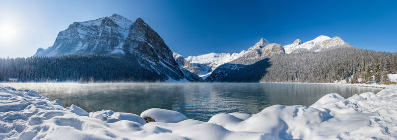 Frozen lake by snowcapped mountains against sky