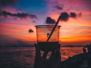 Low angle view of beer glass on beach against sunset sky