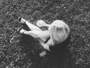 High angle view of young woman holding bottle while sitting on grassy field