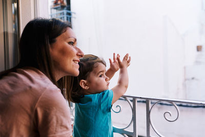 Mother and daughter looking out the window of the house happy