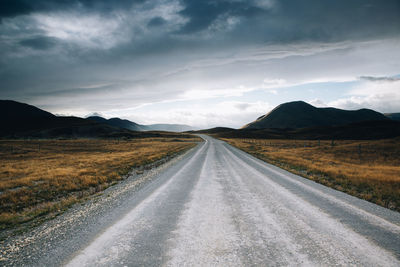 Empty road leading towards mountains against sky