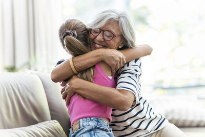 Happy senior woman embracing granddaughter at home