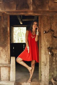 Full length portrait of young woman in red dress standing at abandoned house