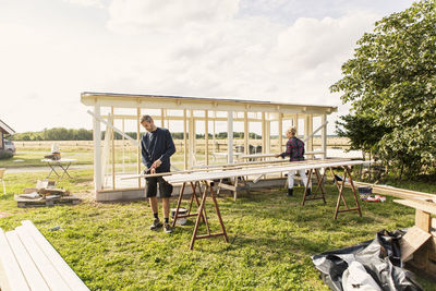 Man and woman making shed at farm against sky