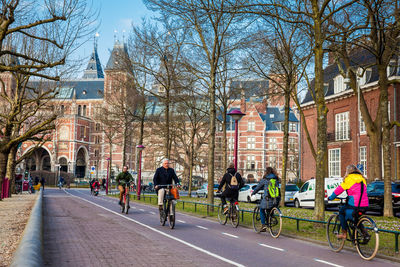 People walking on road along bare trees in city