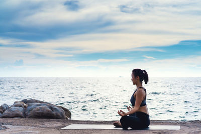 Woman sitting on sea shore against sky