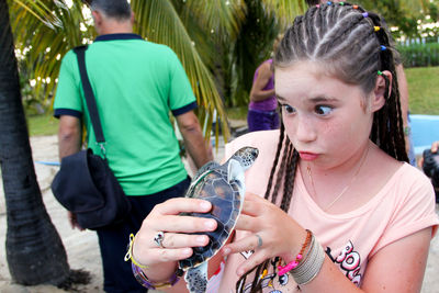 Girl making face while holding turtle at park