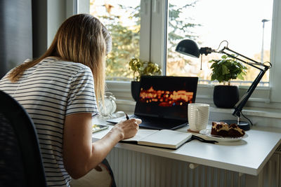 Woman sitting at table by the window and using laptop