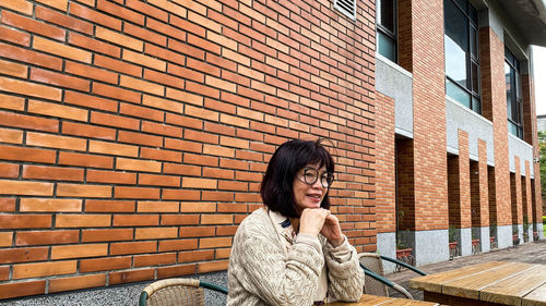 Portrait of woman sitting against brick wall