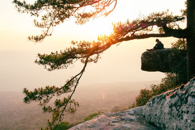 Low angle view of man standing on rock against sky during sunset