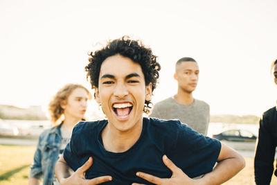 Portrait of happy teenage boy with hands on chest against friends in city