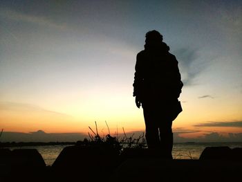 Silhouette man standing at beach against sky during sunset