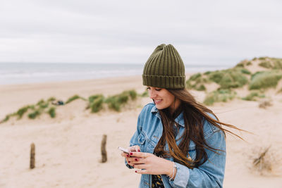 Young woman using mobile phone at beach against sky