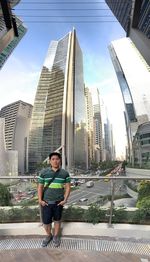 Full length portrait of young man standing against modern buildings