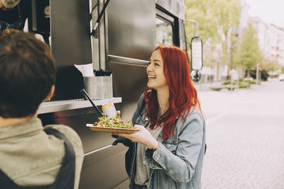 Smiling female customer talking to owner while standing with food plate on street