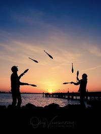 Silhouette men juggling pins at beach against sky during sunset